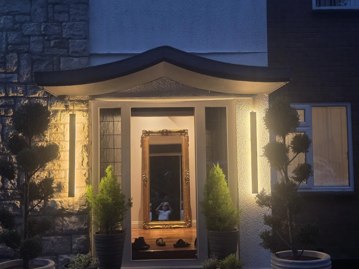 Two vertical outdoor wall lights illuminating a front entrance at dusk