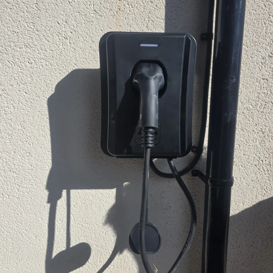 Wall-mounted EV charge point installed on a rendered exterior wall with its charging lead connected