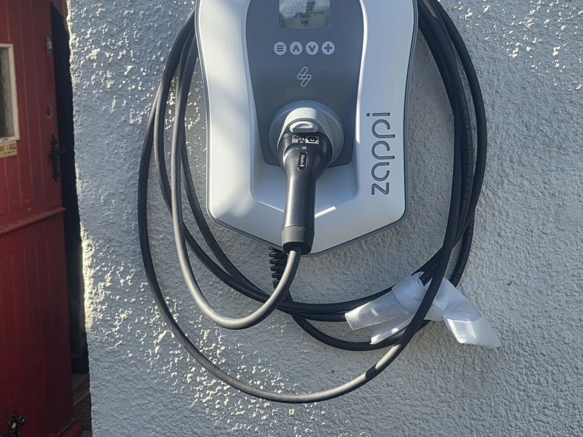Myenergi Zappi EV charger mounted on an exterior wall with its charging cable coiled around the unit