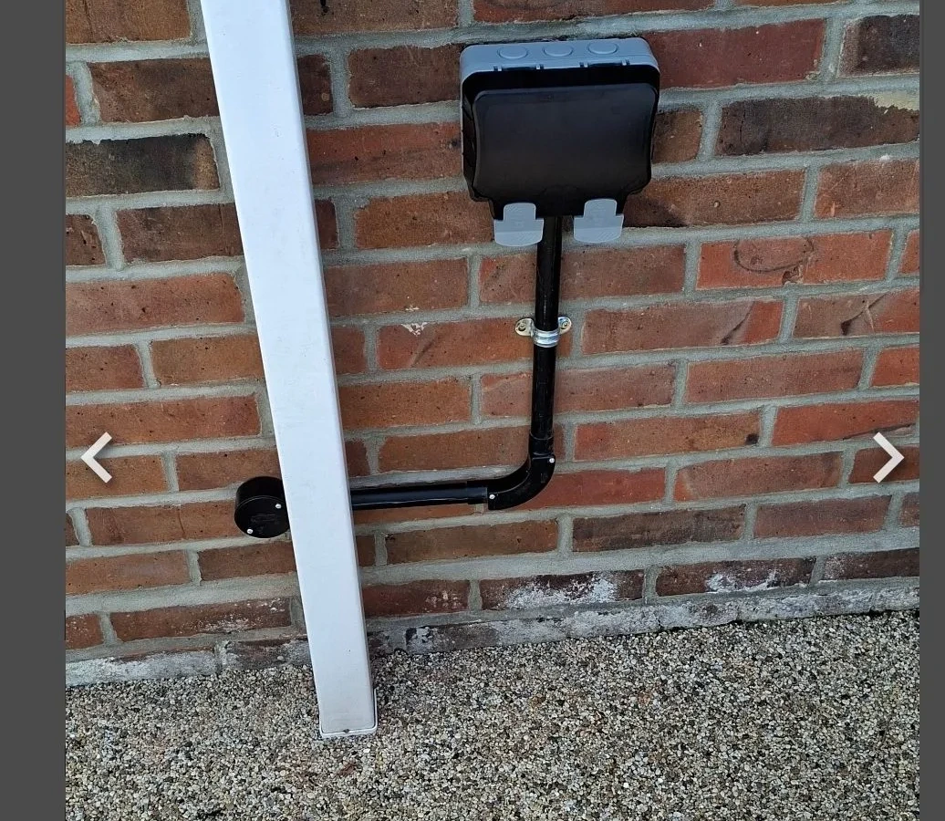 Weatherproof outdoor socket run in black conduit down a brick wall